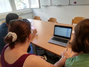 Zwei Frauen und ein Mann sitzen vor einem Laptop - sie schauen auf den Bildschirm.