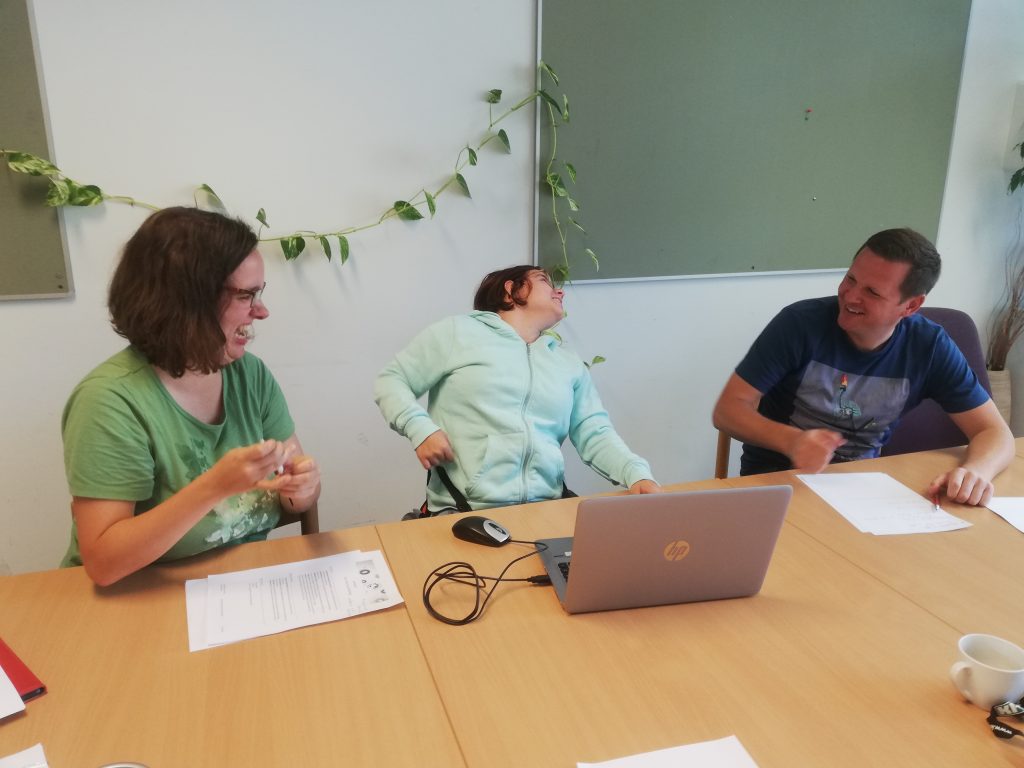 Two women and a man sit together at a laptop and laugh.