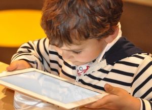 Ein kleiner Junge in einem gestreiften T-Shirt, der etwas auf einem Tablet liest