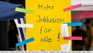 Ein gelbes Blatt Papier mit den Worten 'Mehr Inklusion für alle' mit buntem Tape an eine Scheibe geheftet