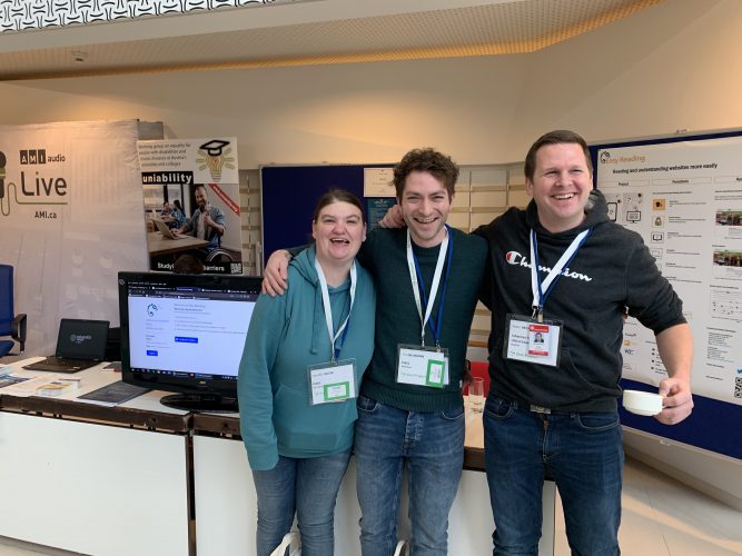 Two men and a woman stand side by side, arm in arm in front of the Easy Reding conference stand. All three of them are laughing.