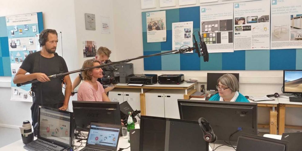 Camera Team films a woman sitting in front of a computer