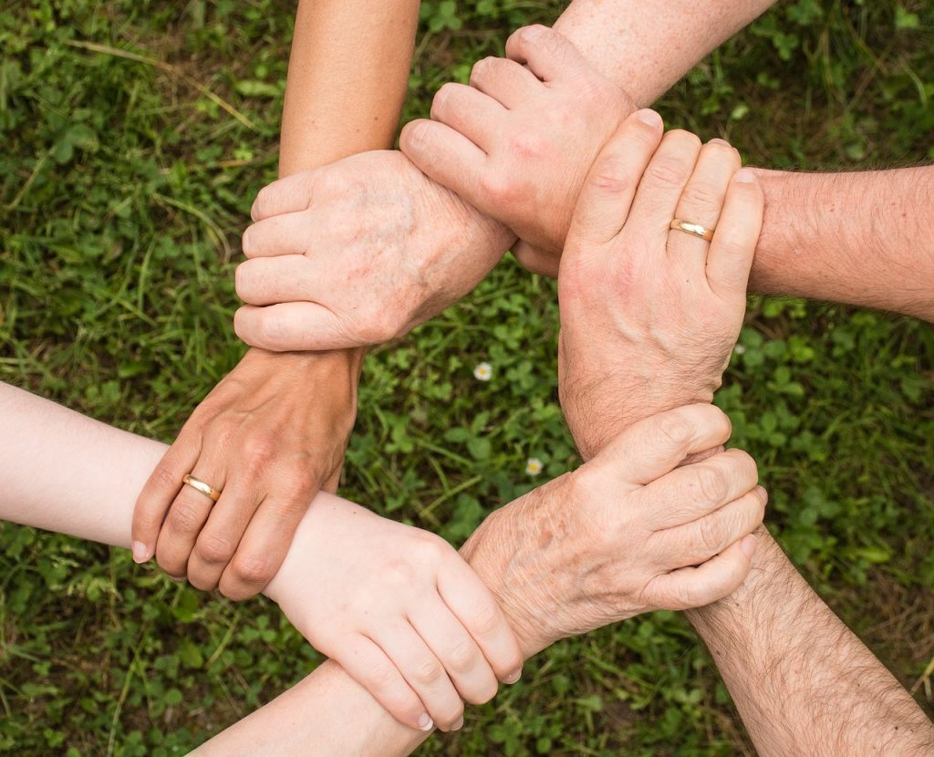 Foto von sechs Händen, die sich gegenseitig an den Handgelenken festhalten und so einen Kreis aus Händen und Armen bilden. 